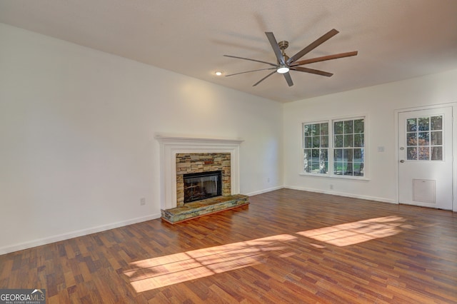 unfurnished living room featuring a stone fireplace, dark wood-type flooring, and ceiling fan