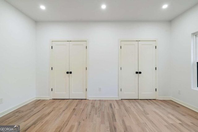 unfurnished bedroom with light hardwood / wood-style flooring and two closets