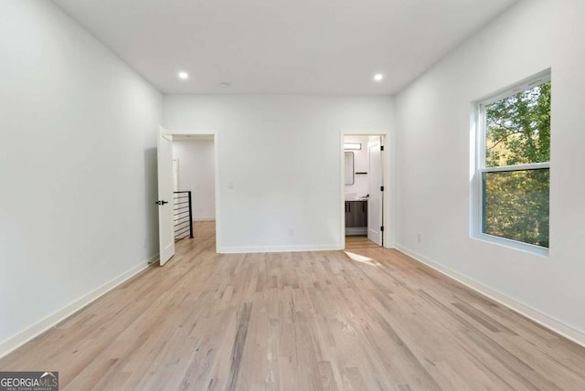 unfurnished bedroom with light hardwood / wood-style floors, multiple windows, and connected bathroom