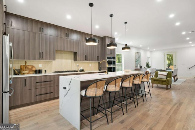 kitchen featuring a wealth of natural light, appliances with stainless steel finishes, hanging light fixtures, and light hardwood / wood-style floors