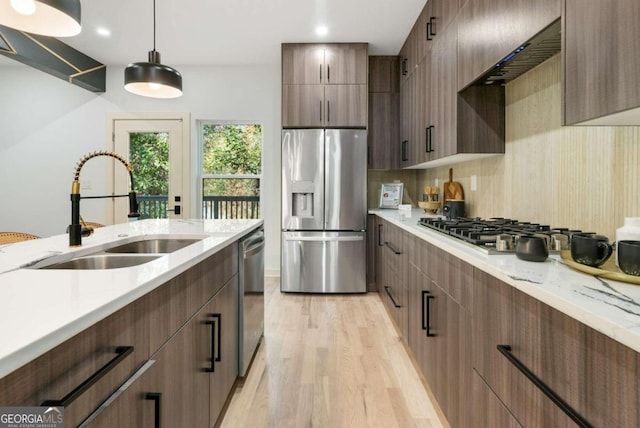 kitchen featuring hanging light fixtures, stainless steel appliances, sink, light stone countertops, and light hardwood / wood-style floors