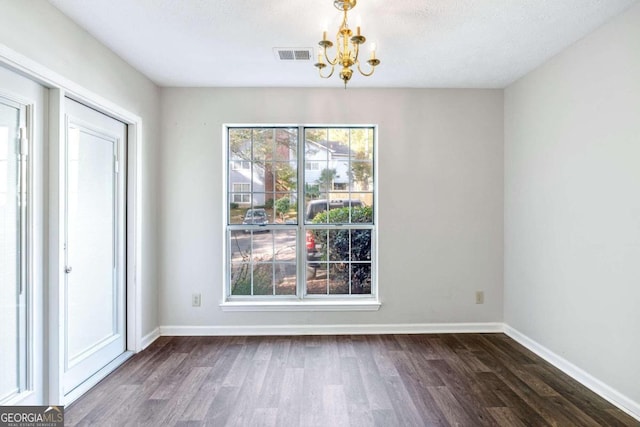 unfurnished dining area with a notable chandelier, a textured ceiling, and dark hardwood / wood-style flooring