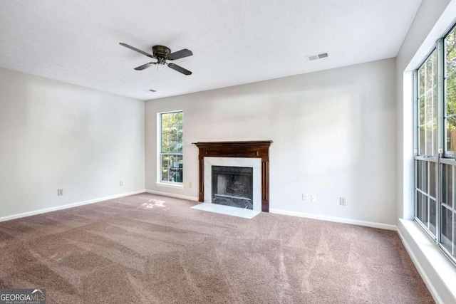 unfurnished living room featuring ceiling fan, a premium fireplace, carpet floors, and plenty of natural light