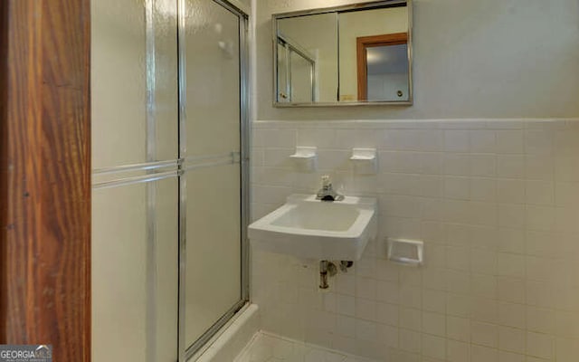 bathroom with sink, a shower with shower door, and tile walls