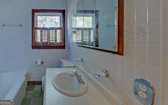 bathroom with a tub to relax in, toilet, tile walls, and sink