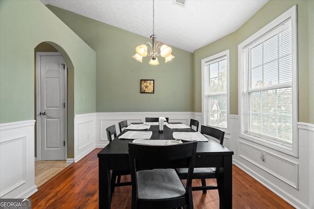 dining space with arched walkways, wainscoting, wood finished floors, vaulted ceiling, and a notable chandelier