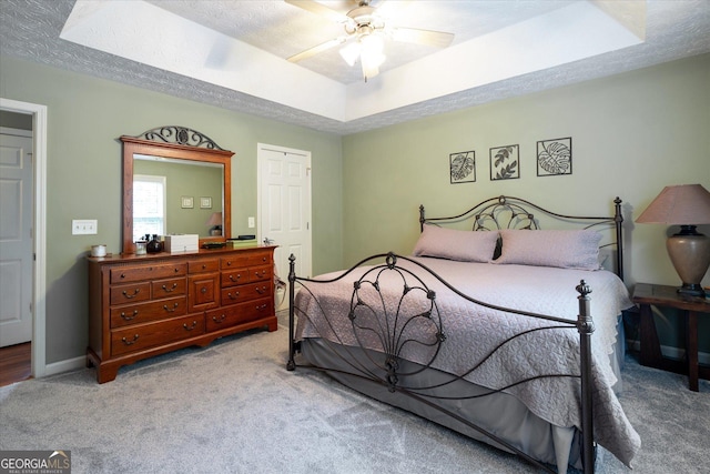 bedroom with a raised ceiling, a textured ceiling, and light colored carpet