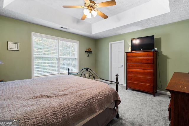 bedroom featuring a textured ceiling, light carpet, visible vents, baseboards, and a tray ceiling