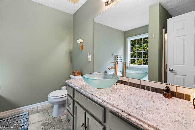 bathroom with a textured ceiling, stone tile flooring, vanity, and baseboards