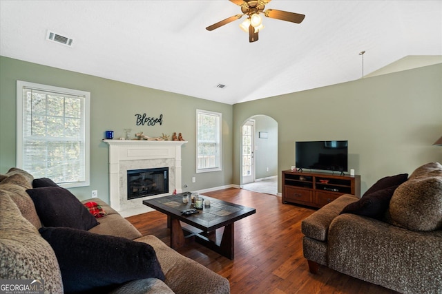 living area with arched walkways, visible vents, a premium fireplace, vaulted ceiling, and wood finished floors