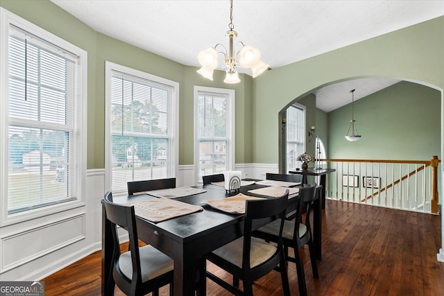 dining area with arched walkways, a wainscoted wall, a notable chandelier, lofted ceiling, and dark wood-type flooring