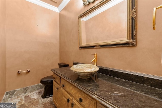 bathroom with toilet, stone finish floor, crown molding, and vanity