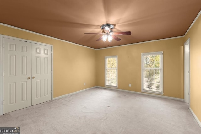 unfurnished bedroom featuring crown molding, a closet, a ceiling fan, carpet flooring, and baseboards