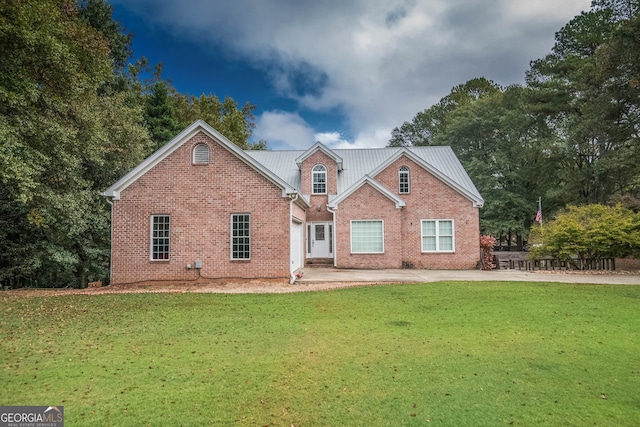 view of front facade with a patio area, brick siding, metal roof, and a front lawn