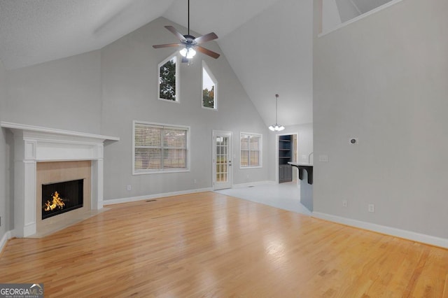 unfurnished living room featuring a textured ceiling, ceiling fan with notable chandelier, light wood-type flooring, and high vaulted ceiling