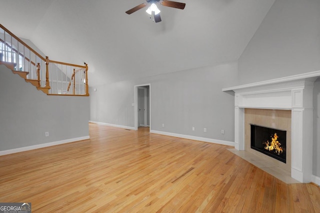 unfurnished living room with a tiled fireplace, high vaulted ceiling, light wood-type flooring, and ceiling fan