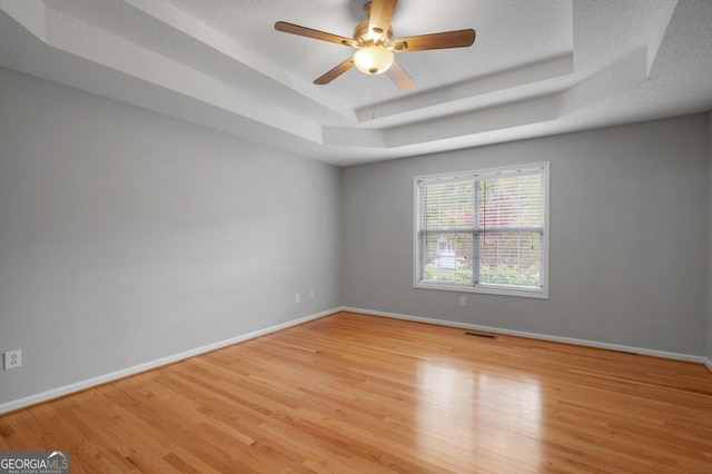 empty room featuring light hardwood / wood-style floors, a textured ceiling, a tray ceiling, and ceiling fan