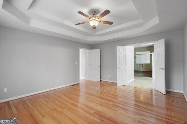 spare room featuring a tray ceiling, light wood-type flooring, and ceiling fan