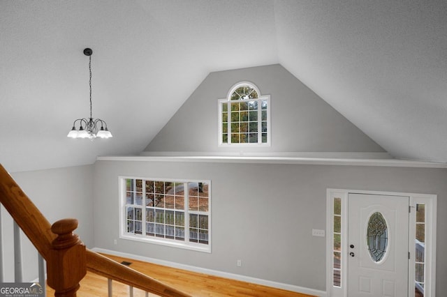 foyer featuring hardwood / wood-style flooring, a textured ceiling, vaulted ceiling, and an inviting chandelier