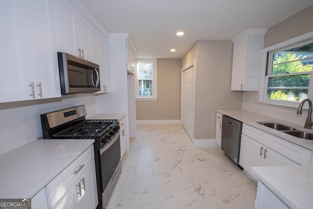 kitchen with sink, appliances with stainless steel finishes, light stone counters, and a healthy amount of sunlight