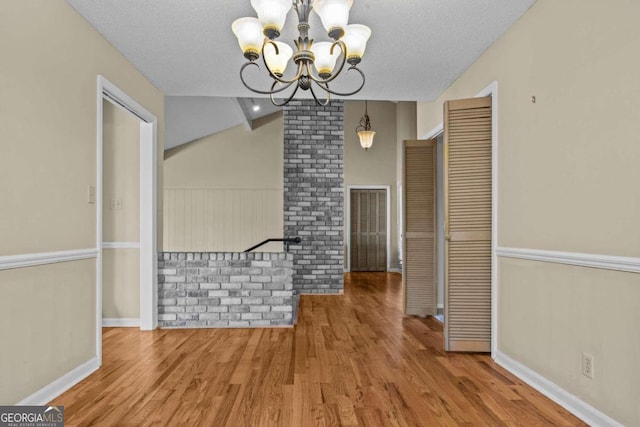 unfurnished dining area with baseboards, a notable chandelier, wood finished floors, and lofted ceiling