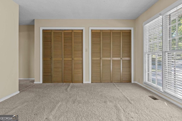 unfurnished bedroom with baseboards, carpet, two closets, and visible vents