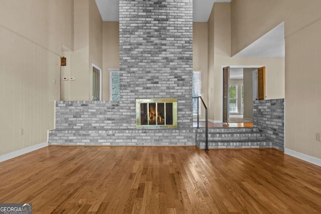 unfurnished living room featuring wood finished floors, baseboards, a brick fireplace, and a high ceiling