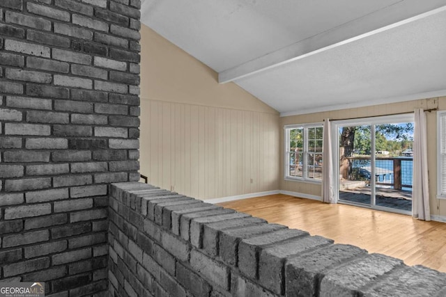 unfurnished living room featuring baseboards, lofted ceiling with beams, wood walls, and wood finished floors
