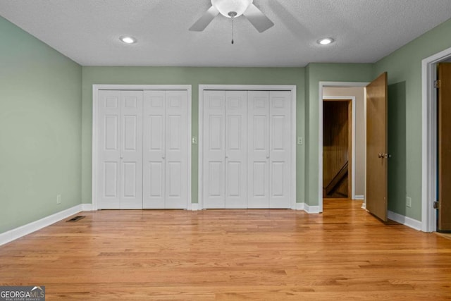 unfurnished bedroom with a textured ceiling, two closets, baseboards, light wood-type flooring, and visible vents