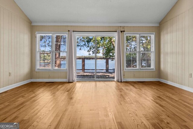 interior space with wooden walls, baseboards, vaulted ceiling, and light wood finished floors