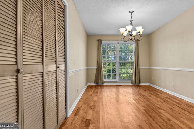 unfurnished dining area with a textured ceiling, baseboards, a notable chandelier, and wood finished floors