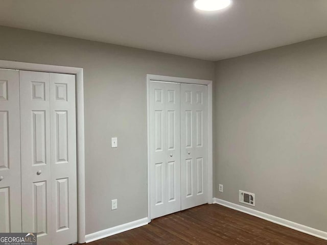 unfurnished bedroom featuring two closets and dark wood-type flooring