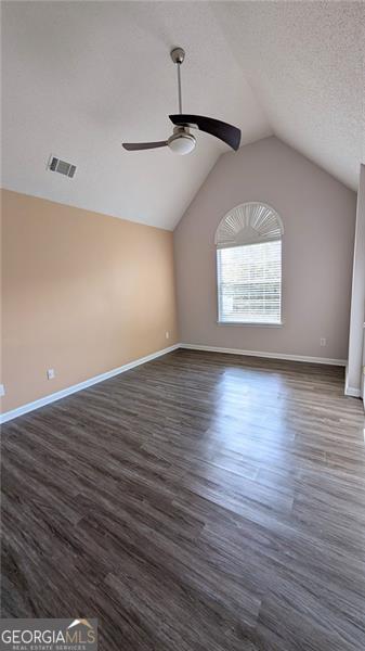 unfurnished room with a textured ceiling, lofted ceiling, dark hardwood / wood-style floors, and ceiling fan