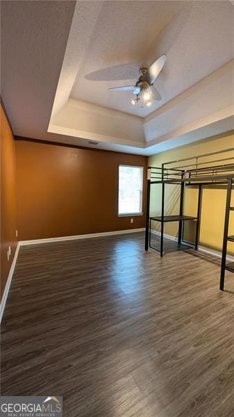 unfurnished bedroom with a tray ceiling, dark hardwood / wood-style floors, and crown molding