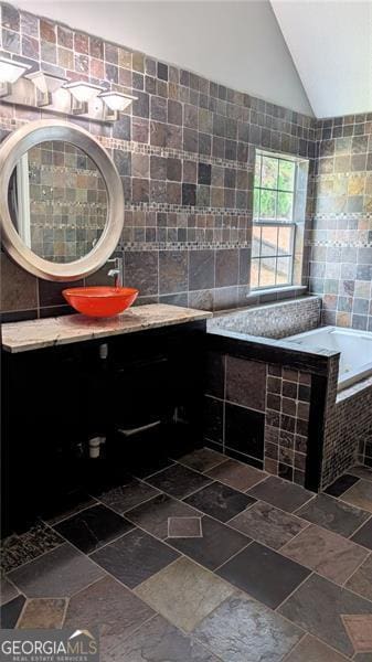 bathroom featuring lofted ceiling, vanity, tiled bath, and tile walls