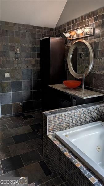 bathroom featuring sink, tile walls, vaulted ceiling, and tiled bath