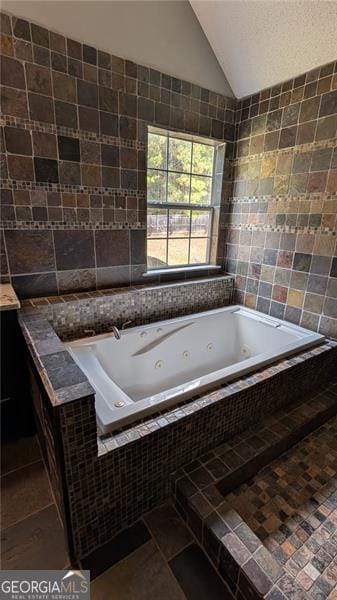 bathroom with vaulted ceiling, tile patterned flooring, tiled bath, and tile walls