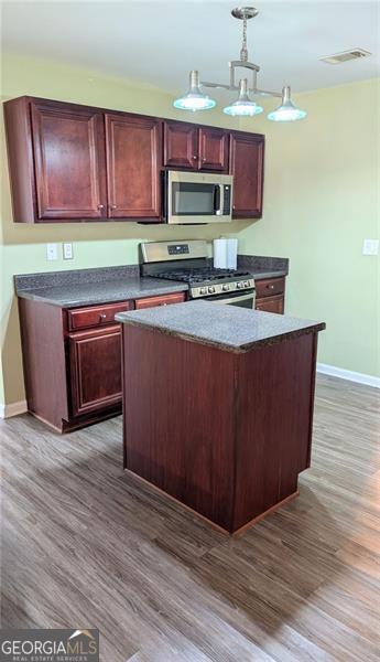 kitchen featuring dark wood-type flooring, pendant lighting, appliances with stainless steel finishes, and a center island