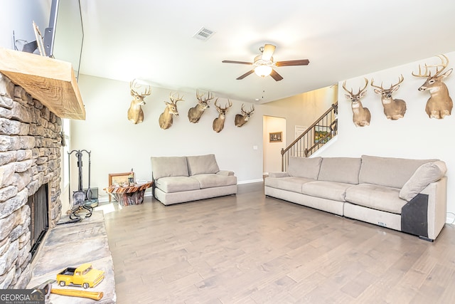 living room with a stone fireplace, wood-type flooring, and ceiling fan