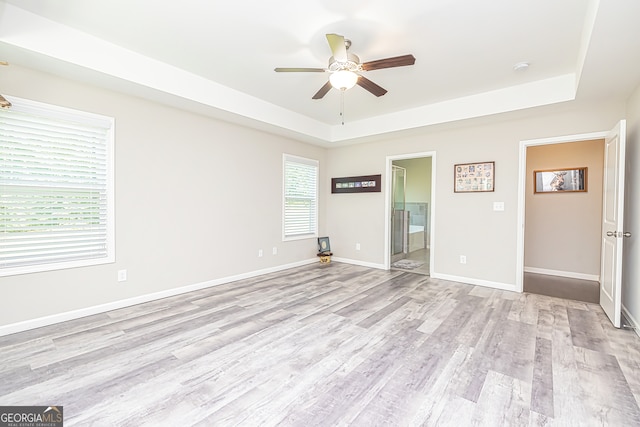 interior space with light hardwood / wood-style flooring, ensuite bathroom, a raised ceiling, and ceiling fan