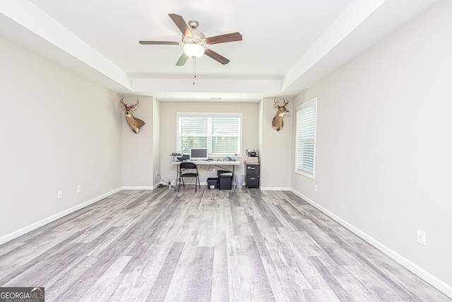 unfurnished office with ceiling fan, a raised ceiling, and light wood-type flooring