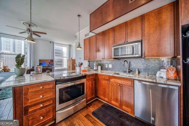 kitchen featuring dark wood-type flooring, kitchen peninsula, stainless steel appliances, sink, and light stone counters