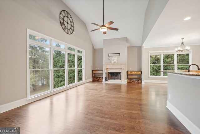 unfurnished living room with hardwood / wood-style floors, high vaulted ceiling, sink, and ceiling fan with notable chandelier