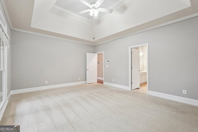 unfurnished bedroom with ensuite bath, ornamental molding, light colored carpet, a raised ceiling, and ceiling fan