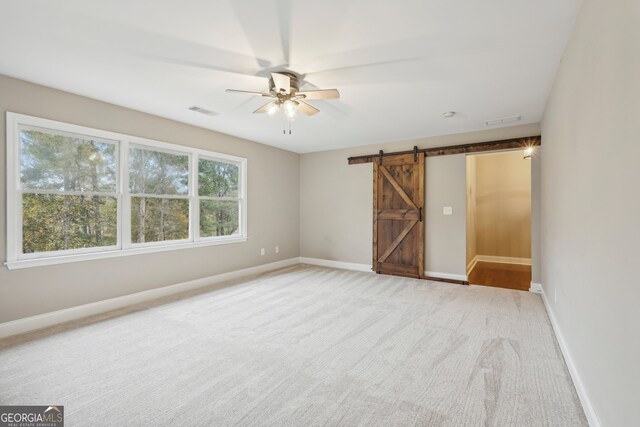 unfurnished room with a barn door, light colored carpet, and ceiling fan