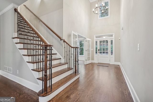 entrance foyer with an inviting chandelier, dark wood-type flooring, a towering ceiling, and french doors