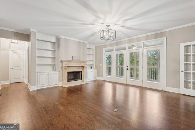 unfurnished living room featuring french doors, dark wood-type flooring, ornamental molding, an inviting chandelier, and built in features