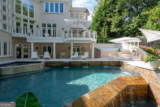 rear view of house with french doors, a pool with hot tub, pool water feature, a balcony, and a patio area