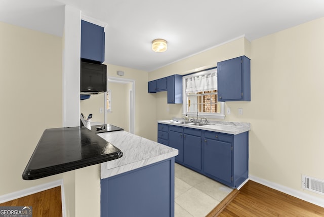 kitchen featuring kitchen peninsula, a kitchen bar, light wood-type flooring, sink, and blue cabinets