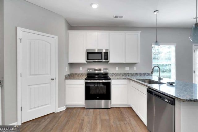 kitchen with appliances with stainless steel finishes, light wood-type flooring, sink, white cabinets, and hanging light fixtures